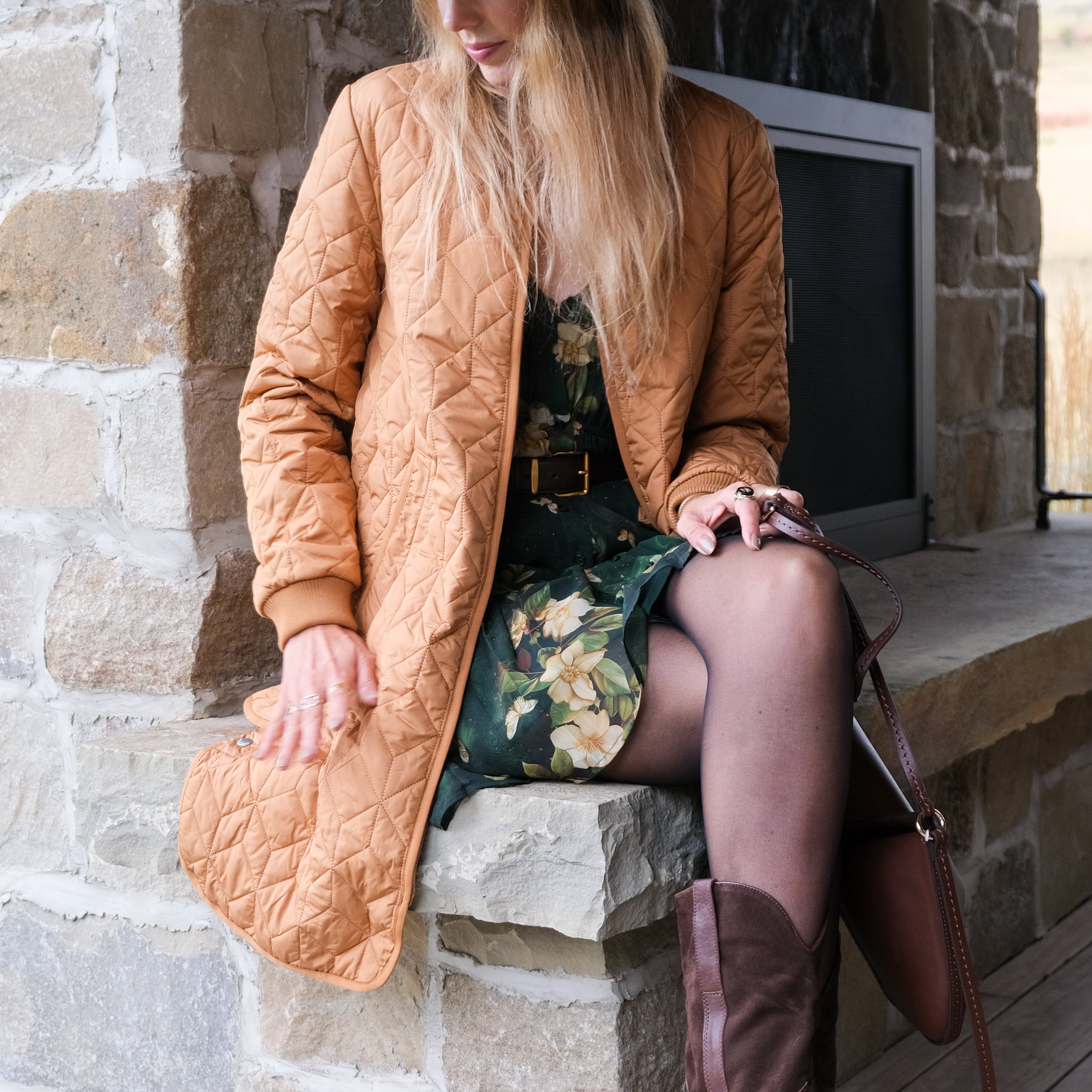 Woman in a tan coat and brown boots sitting on stone steps.