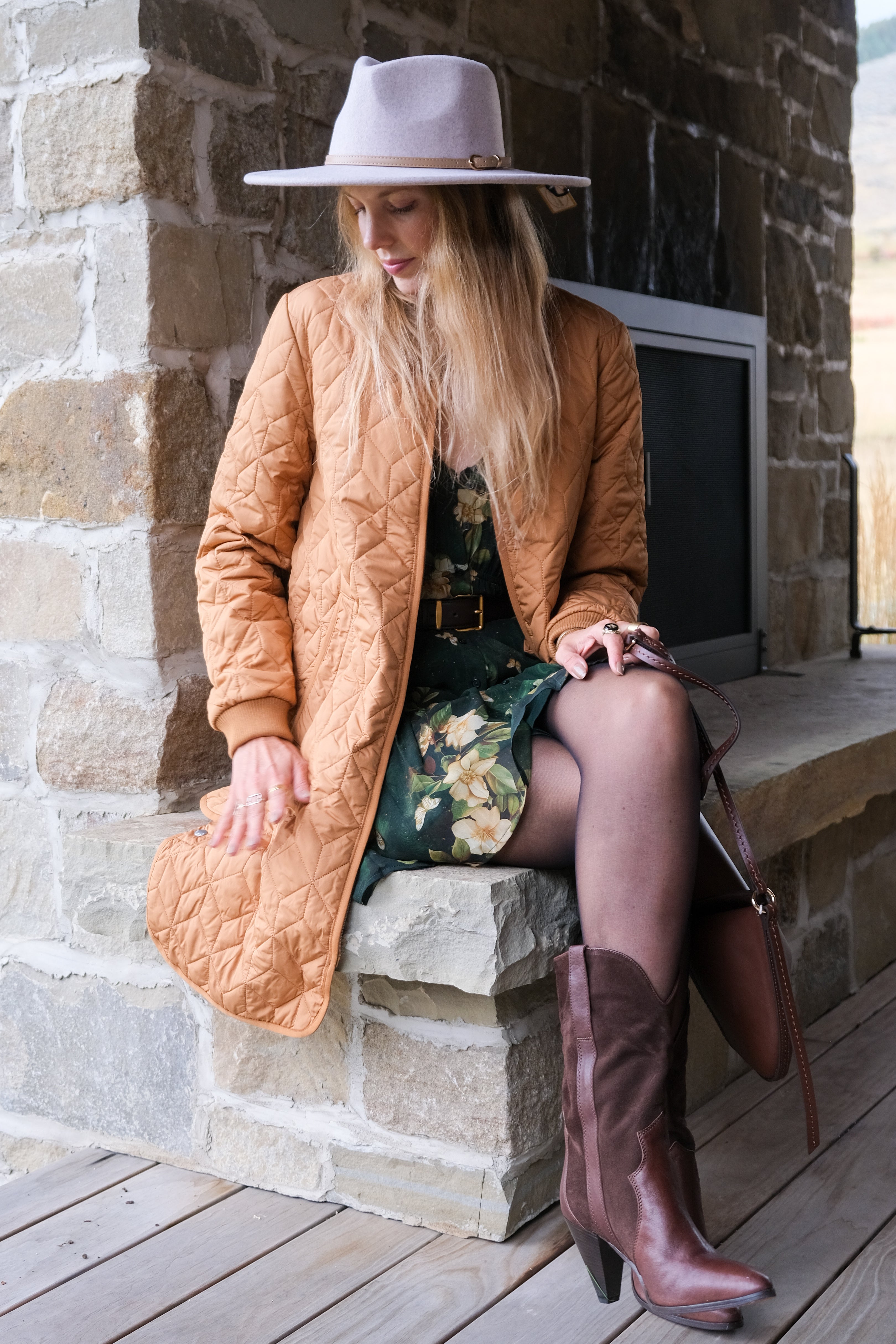 Woman in a tan coat and brown boots sitting on stone steps.